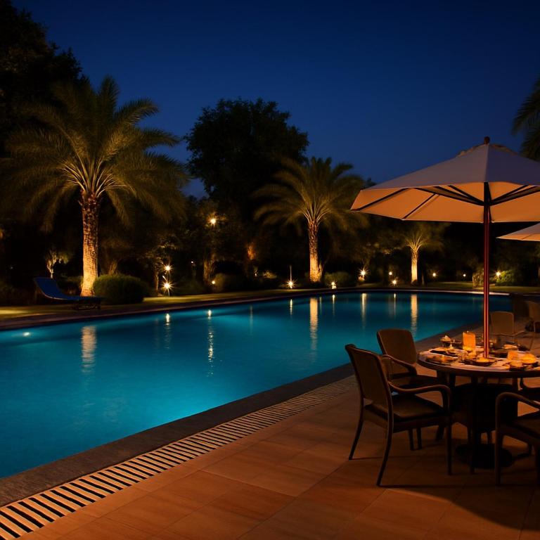 a table with an umbrella next to a swimming pool at night at The Mayur Resort # Big Swimming Pool # Luxury Rooms # Garden # Playing Zone # Away From City Hustle # Property Of The Year # By Elegance # in Vrindāvan