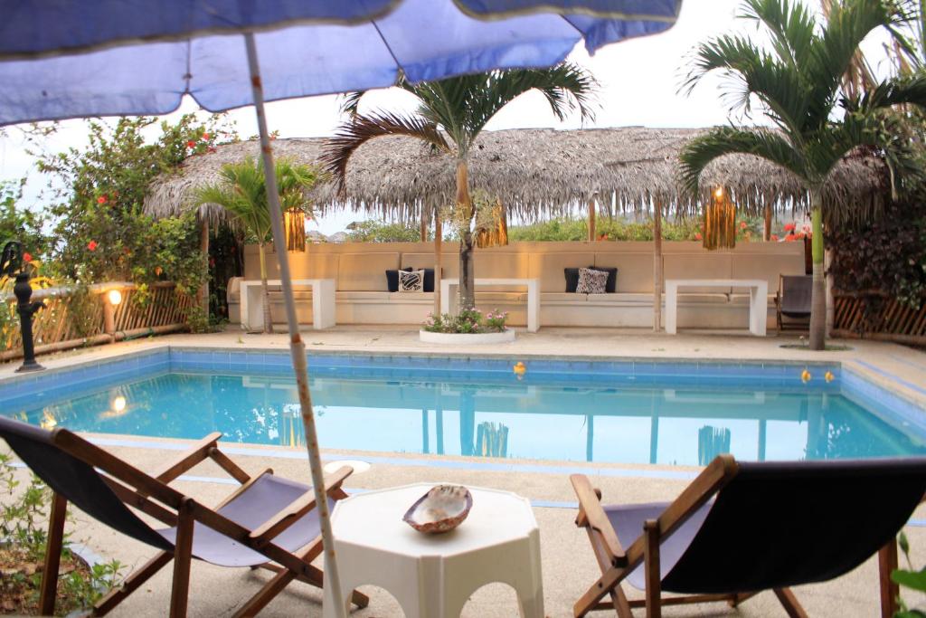 a swimming pool with two chairs and an umbrella at Viejamar B&B in Puerto López