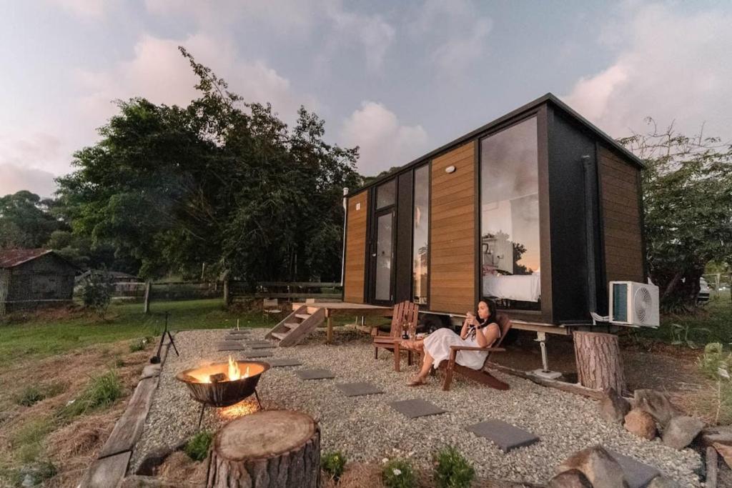 a woman sitting in a chair outside of a tiny house at Rainforest Sunsets by Tiny Away in Kuranda