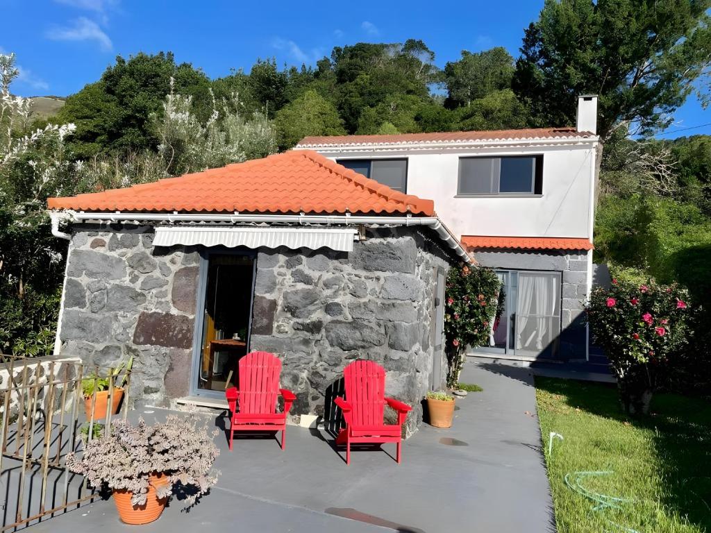 a house with two red chairs and a building at Casa da Petra in Urzelina