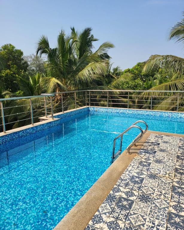 a swimming pool with blue water and palm trees at Calangute house inn in Calangute