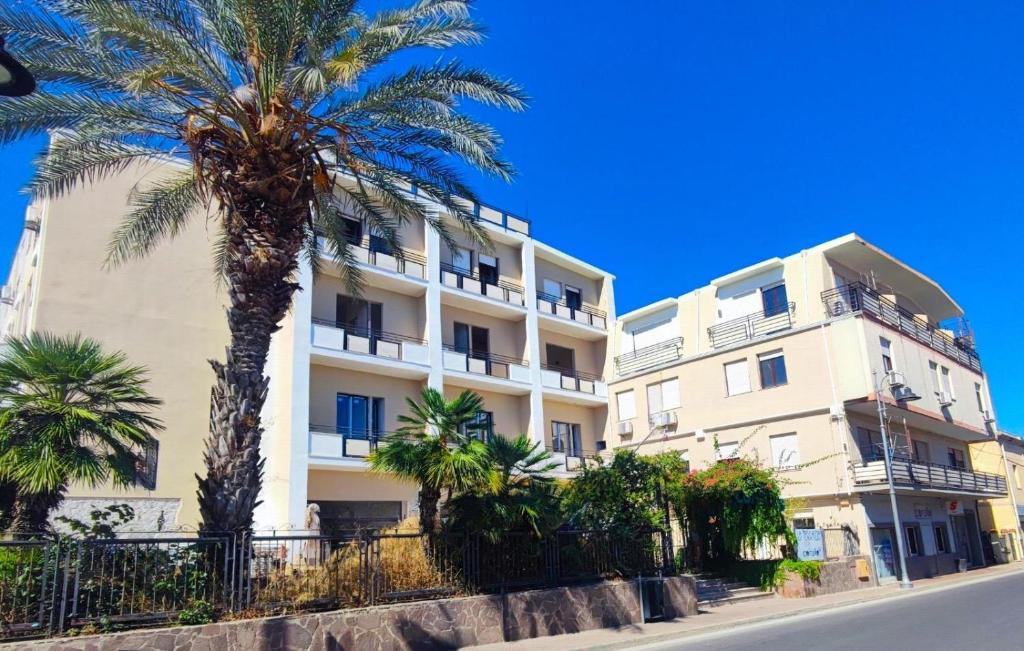 a tall white building with palm trees in front of it at Hotel Corallo New in Muravera