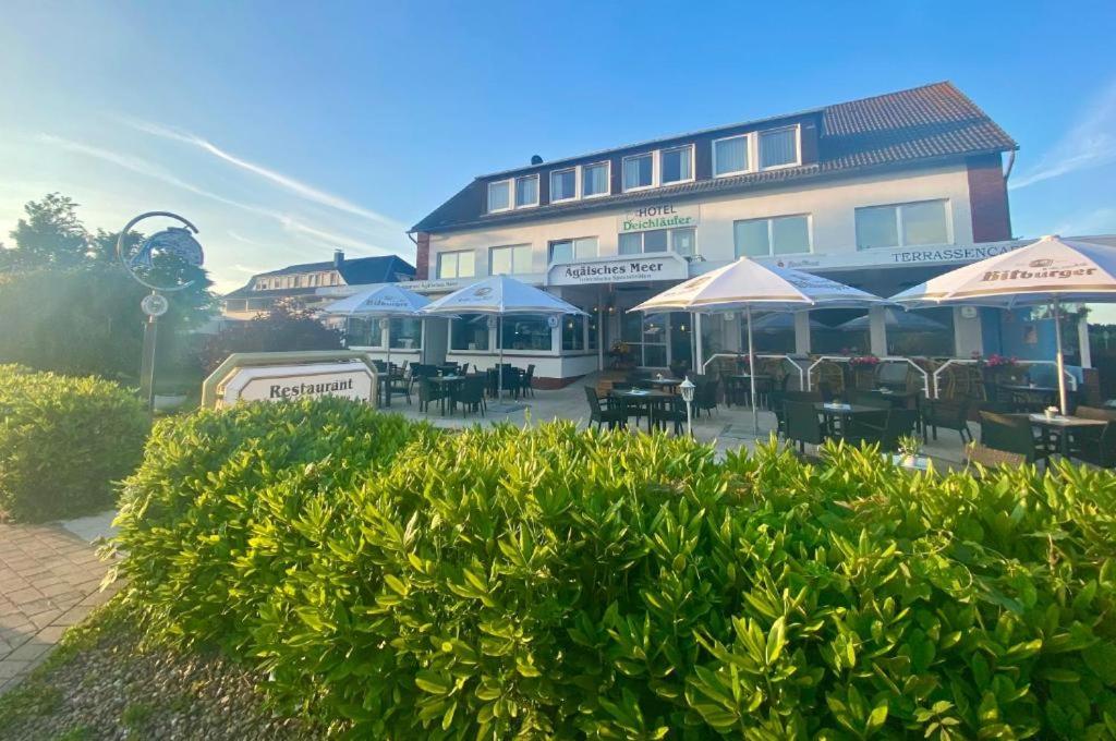 a building with tables and umbrellas in front of it at Strandhotel Deichläufer in Butjadingen