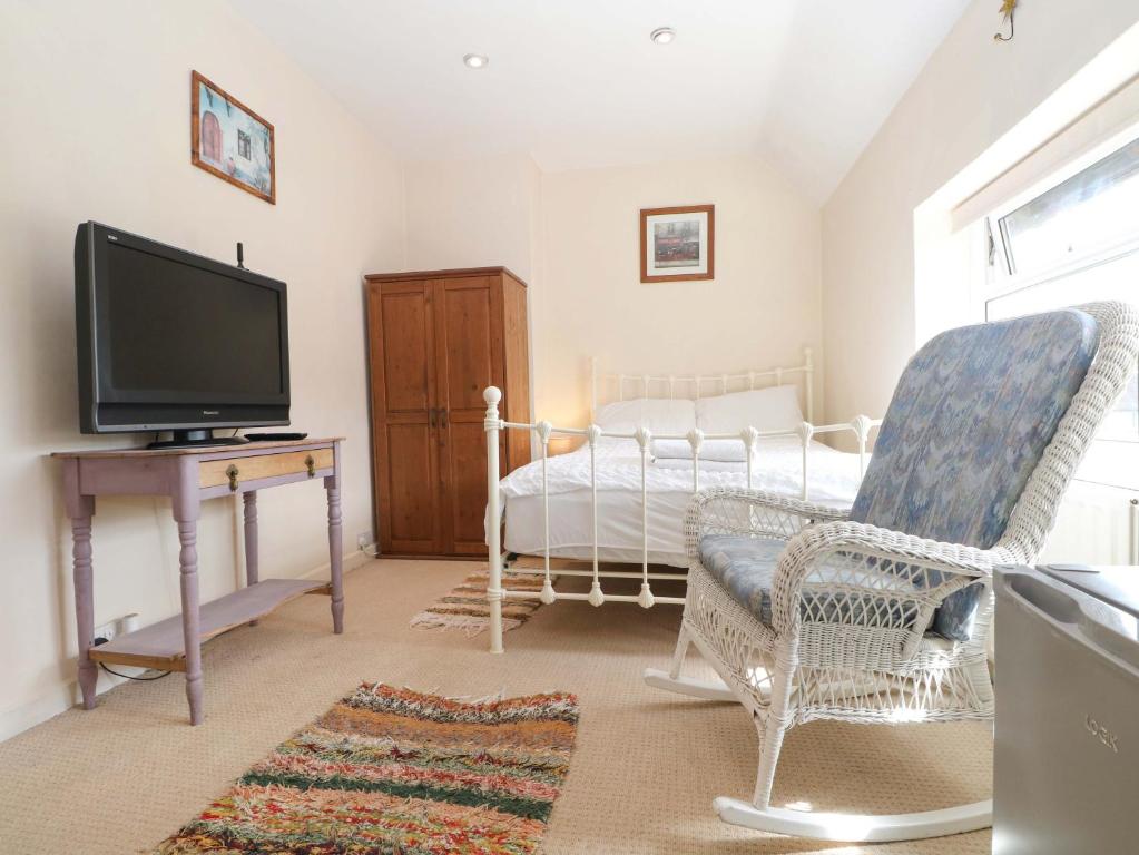 a living room with a tv and a chair and a bed at Daisy Cottage in Dorking