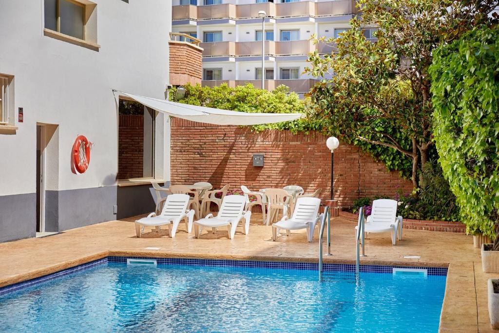 a pool with white chairs and a table and a umbrella at Apartamentos Eldorado in Lloret de Mar