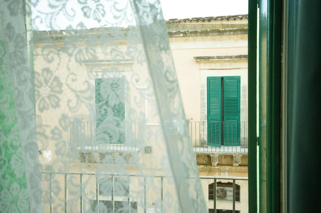 a window with a view of a building with green shutters at BIANCA ROOMS in Noto