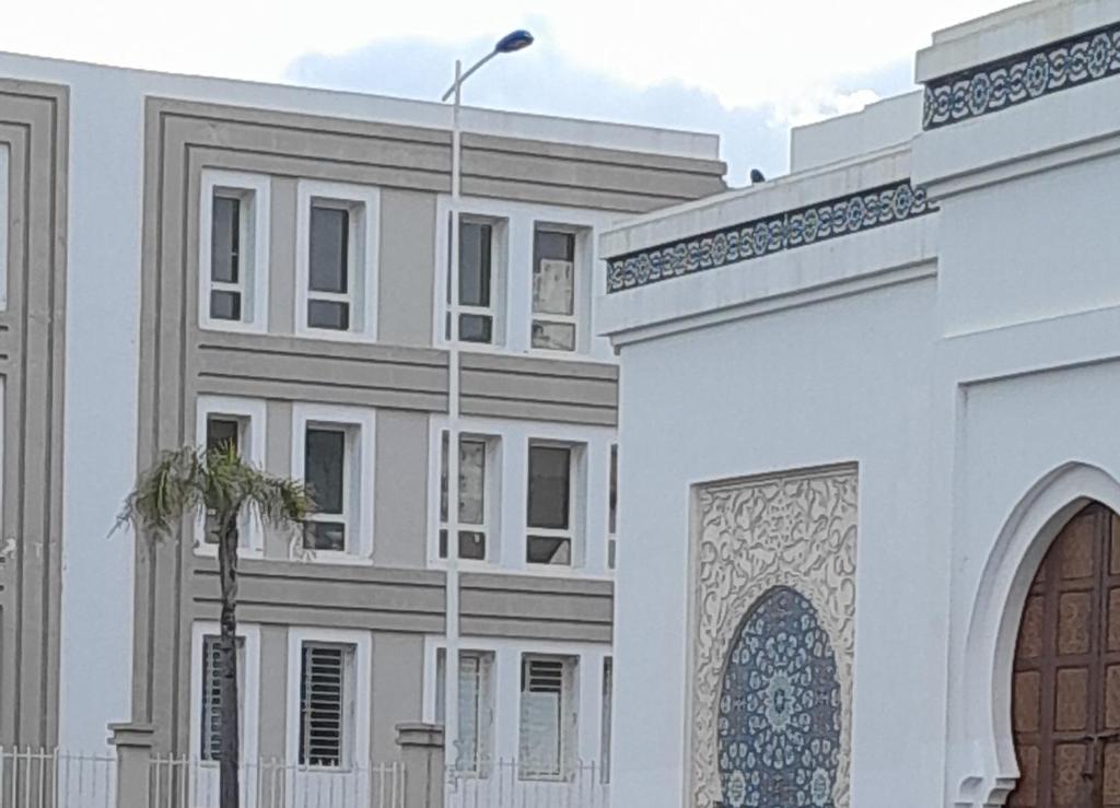a white building with a gate and a palm tree at سيدي رحال الشاطئ in Sidi Rahal