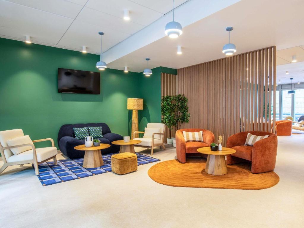 a lobby with chairs and tables and a green wall at Adagio Access Paris Nanterre in Nanterre