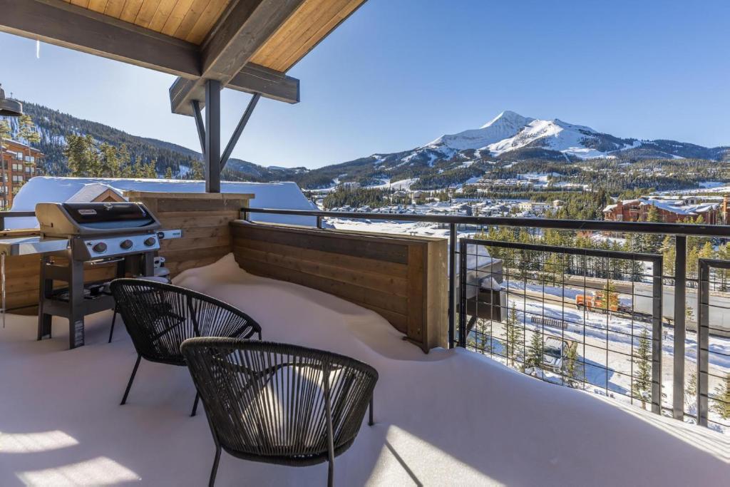 a balcony with a grill and chairs and mountains at Mountain Lake Condo - Unit 502B in Big Sky