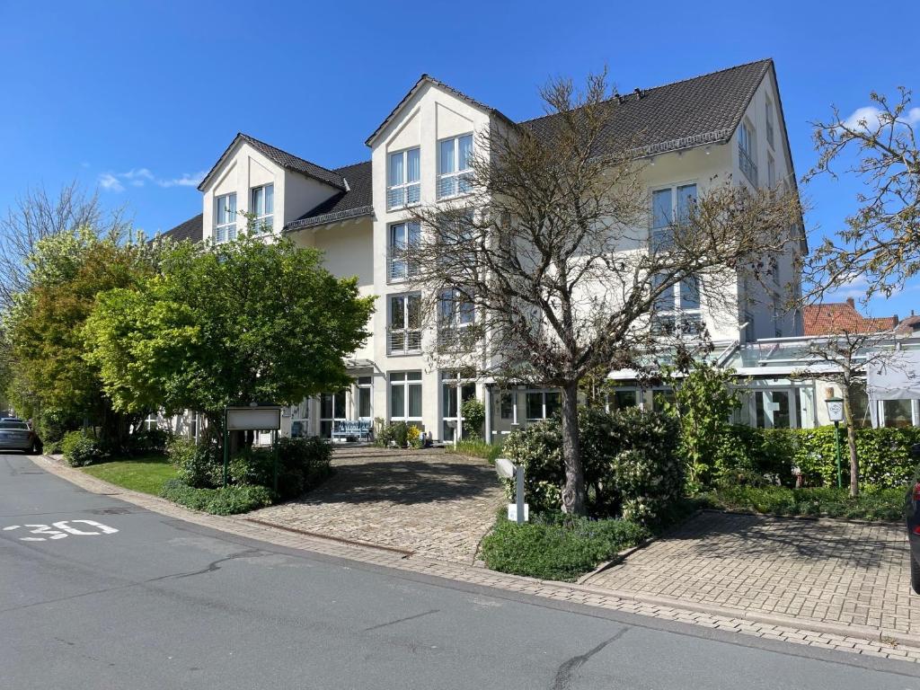 a white house with a tree in front of a street at pepb Schulungshotel in Sarstedt
