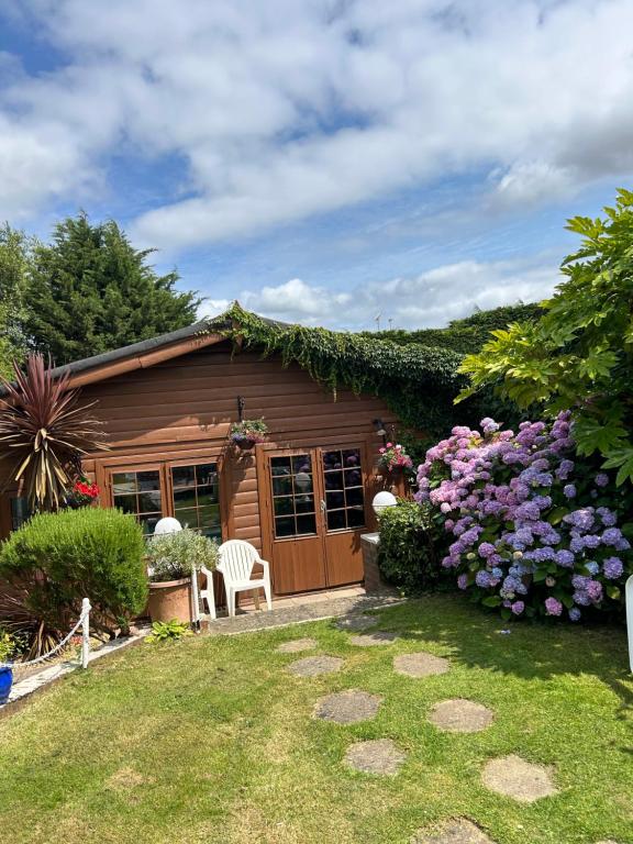 a wooden cabin with purple flowers in the yard at Silverleigh Spa LTD in Fawkham