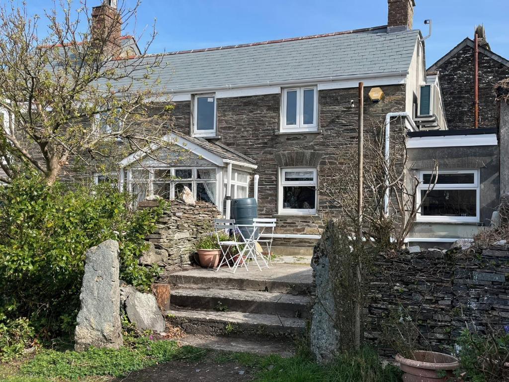 a stone house with a table and a chair on the porch at Sunnybrae Cottage in Tintagel