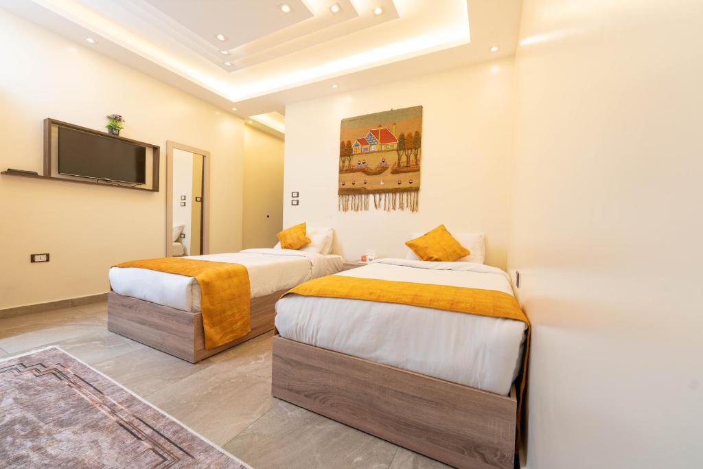 two beds in a room with a tv on the wall at Petra Pyramids View in Al Kawāmil Qiblī