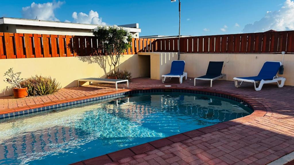 a swimming pool with two blue chairs and a patio at Ensuite Condo Aruba in Palm-Eagle Beach