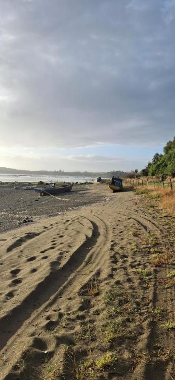 a dirt road with a boat on a beach at Luz de mareas in Ancud