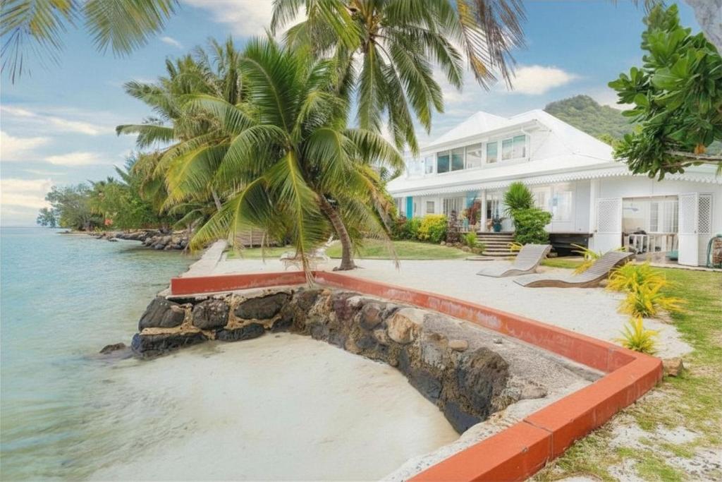 a white house with a palm tree in front of the water at Luxurious 4BR Villa in Vairoa