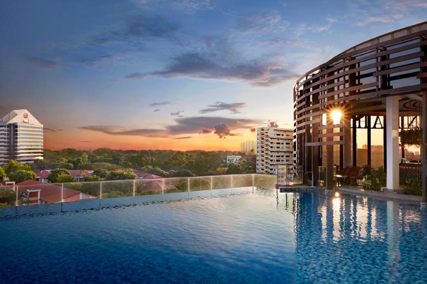 a hotel swimming pool with a sunset in the background at Momentus Hotel Alexandra in Singapore