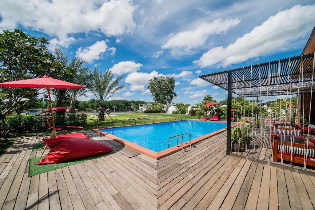 a pool with a red umbrella next to a wooden deck at The Campster Kanchanaburi in Kanchanaburi City