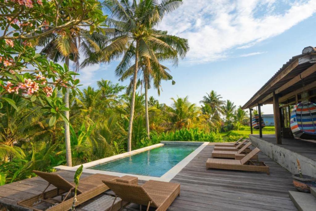 an outdoor deck with a swimming pool and palm trees at Harmony Heaven Ubud by The Travel Ubud Bali in Ubud