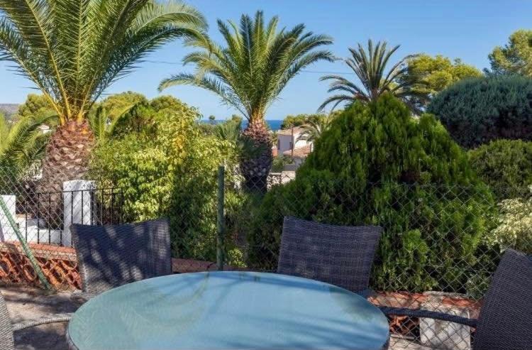 a glass table and chairs on a patio with palm trees at villa cap marti in El Tosalet