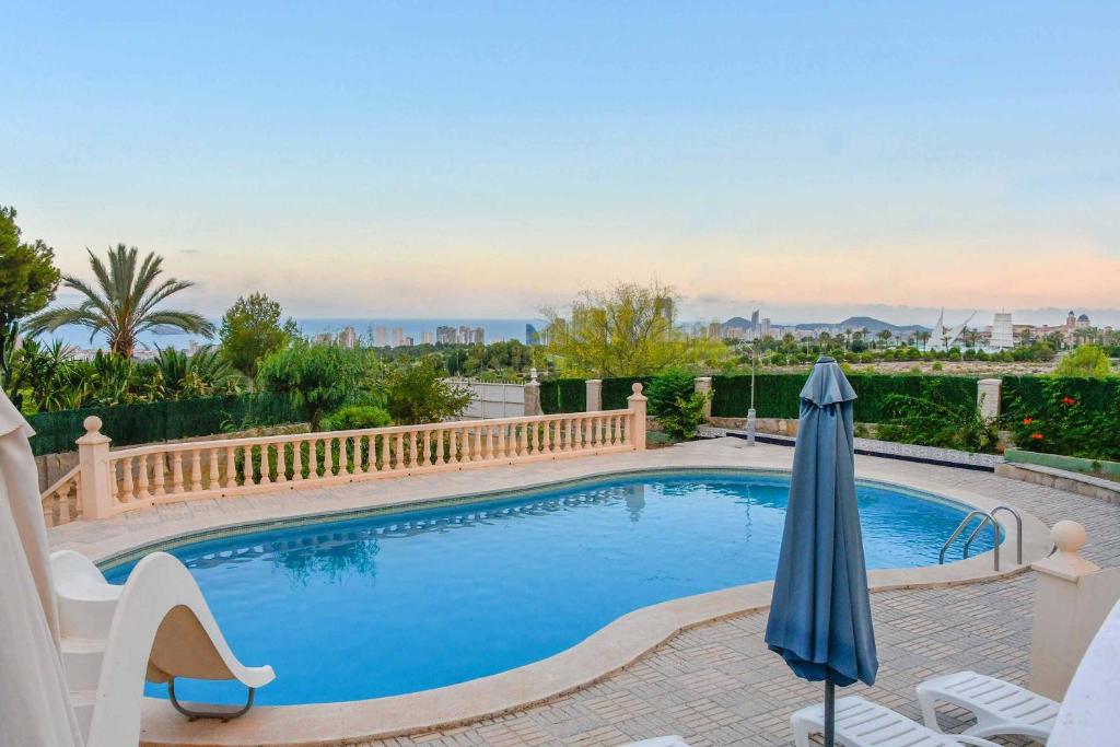 a swimming pool with an umbrella and chairs on a patio at Villa Carousel in Benidorm