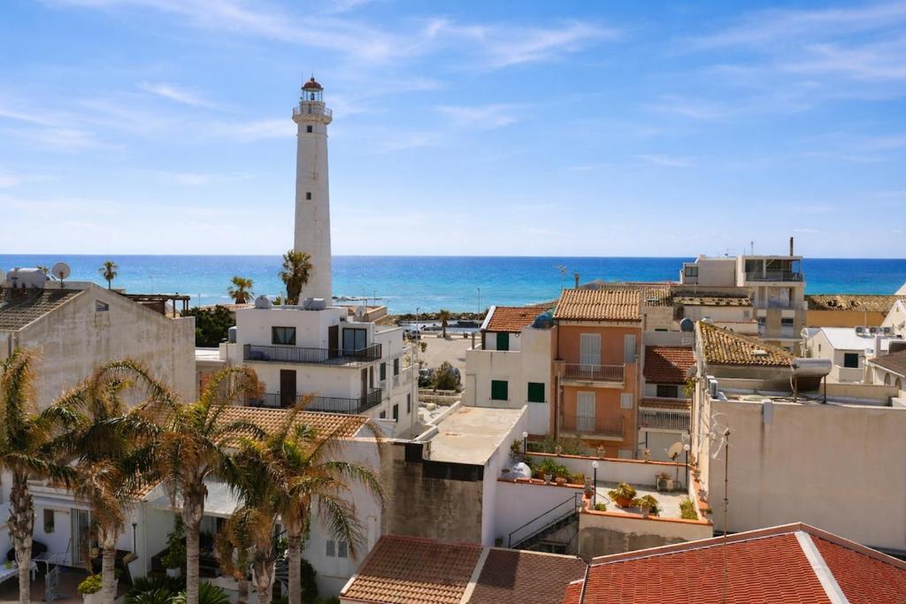 a lighthouse in a city with buildings and the ocean at Seafront Iconic Lighthouse View Punta Secca in Punta Secca