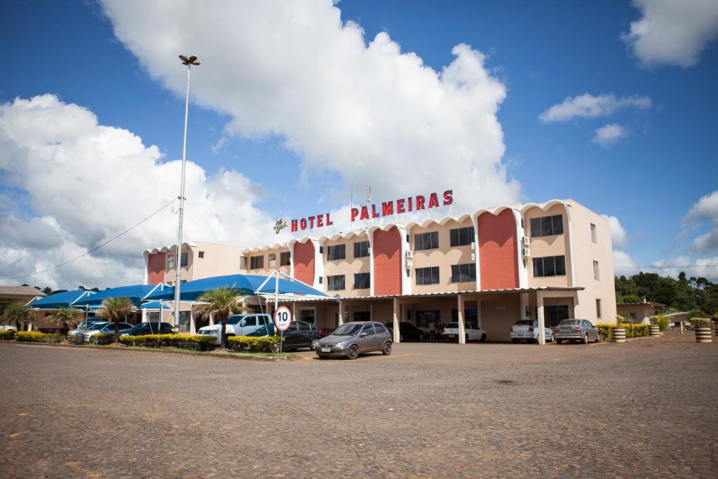 un gran edificio con coches estacionados en un estacionamiento en Hotel Palmeiras, en Laranjeiras do Sul