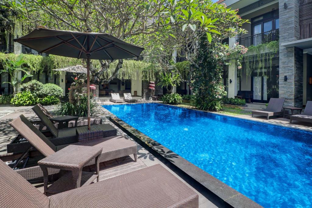 a swimming pool with chairs and an umbrella next to a building at Palette Resort Argya Santi Jimbaran in Jimbaran