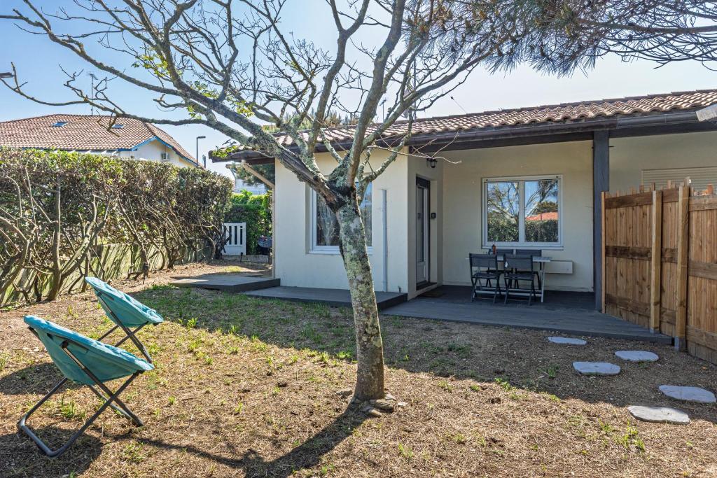 a house with a tree and two chairs in the yard at L'Echo des Vagues -Conciergerieland in Vieux-Boucau-les-Bains