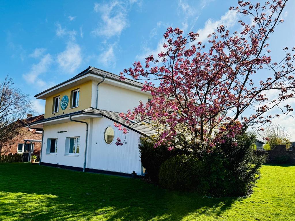 a white house with a tree with pink flowers at Die Schlafstube - Boutiquehotel in Neuharlingersiel