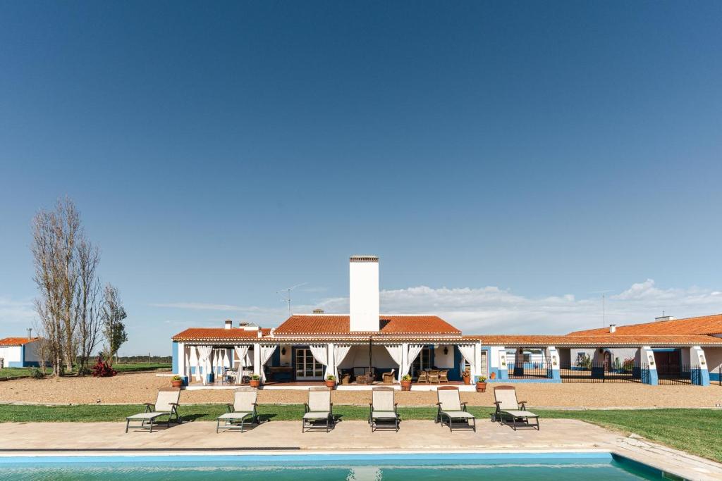 a building with chairs and a pool in front of it at Charming Farm House With Pool in Ferreira do Alentejo