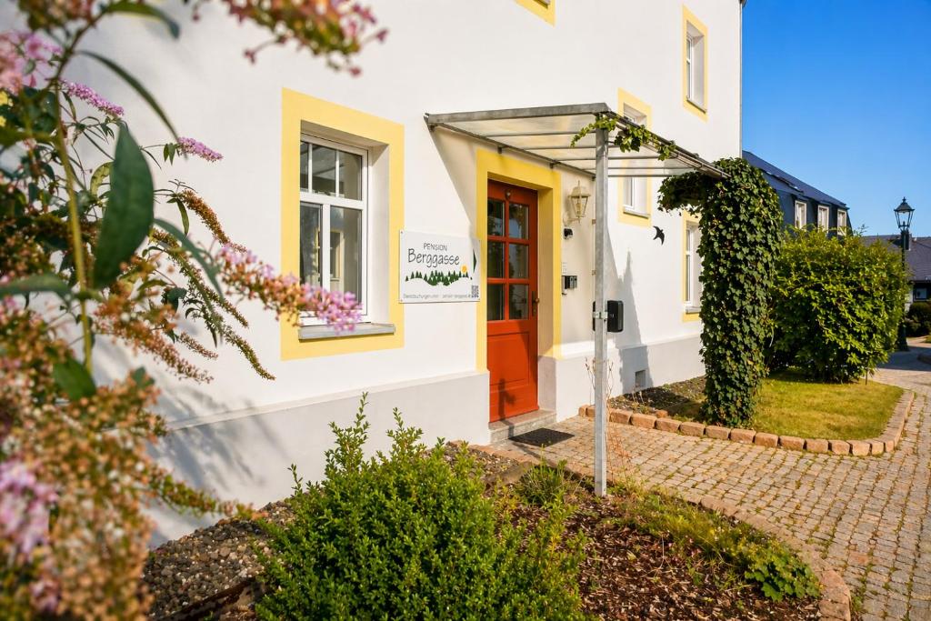 a white house with a red door at Pension Berggasse - Parkplatz, Smart-TV & Küche in Olbernhau