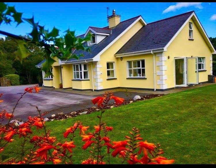 ein gelbes Haus mit roten Blumen im Garten in der Unterkunft Rugged Glen Accommodation in Glengarriff