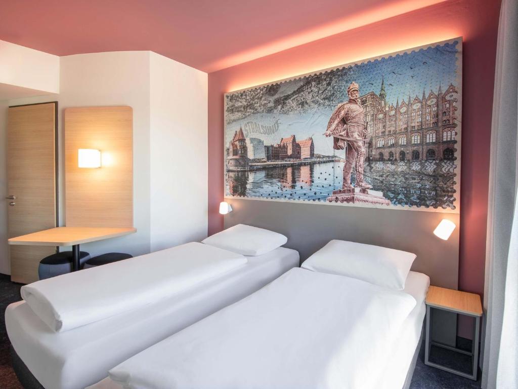 two beds in a room with a painting on the wall at B&B HOTEL Stralsund in Stralsund