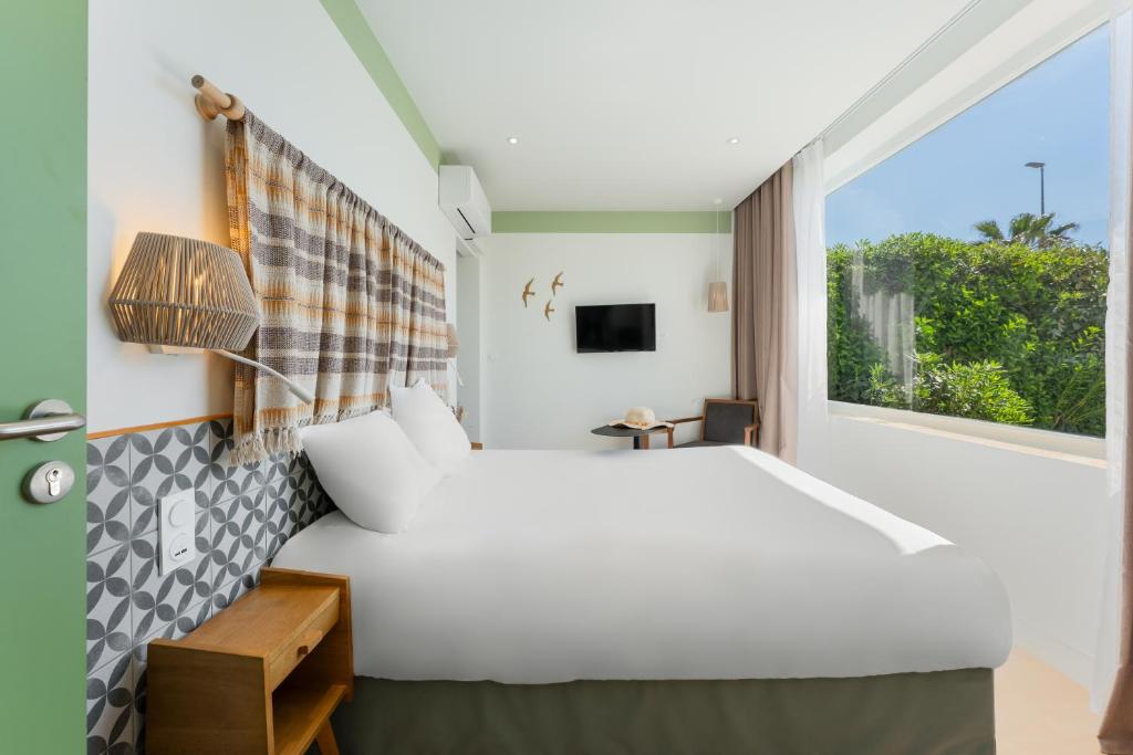 a bedroom with a large white bed and a window at Hôtel du Midi Plage in Palavas-les-Flots