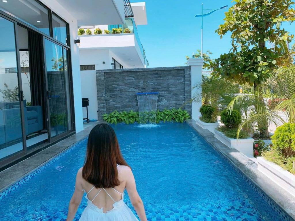 a woman in a white dress standing in front of a swimming pool at FLC Grand Villa BT31-26 in Sầm Sơn