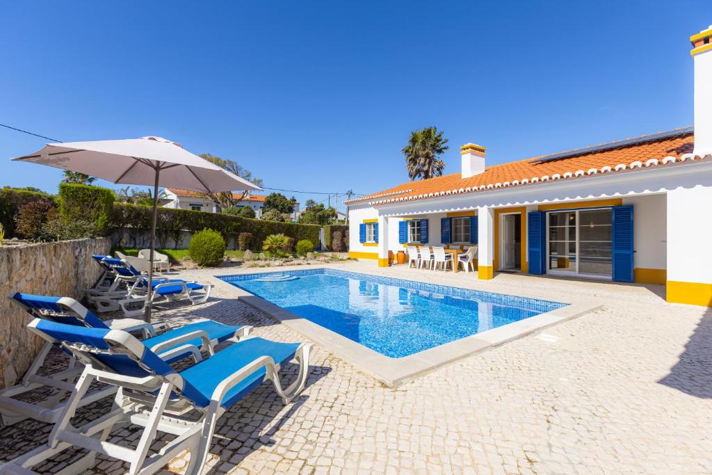 a house with a swimming pool with chairs and an umbrella at Vila Fantastica in Aljezur