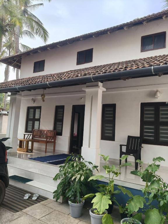 a white house with a porch with plants in front at beach homestay sea view in Kannur