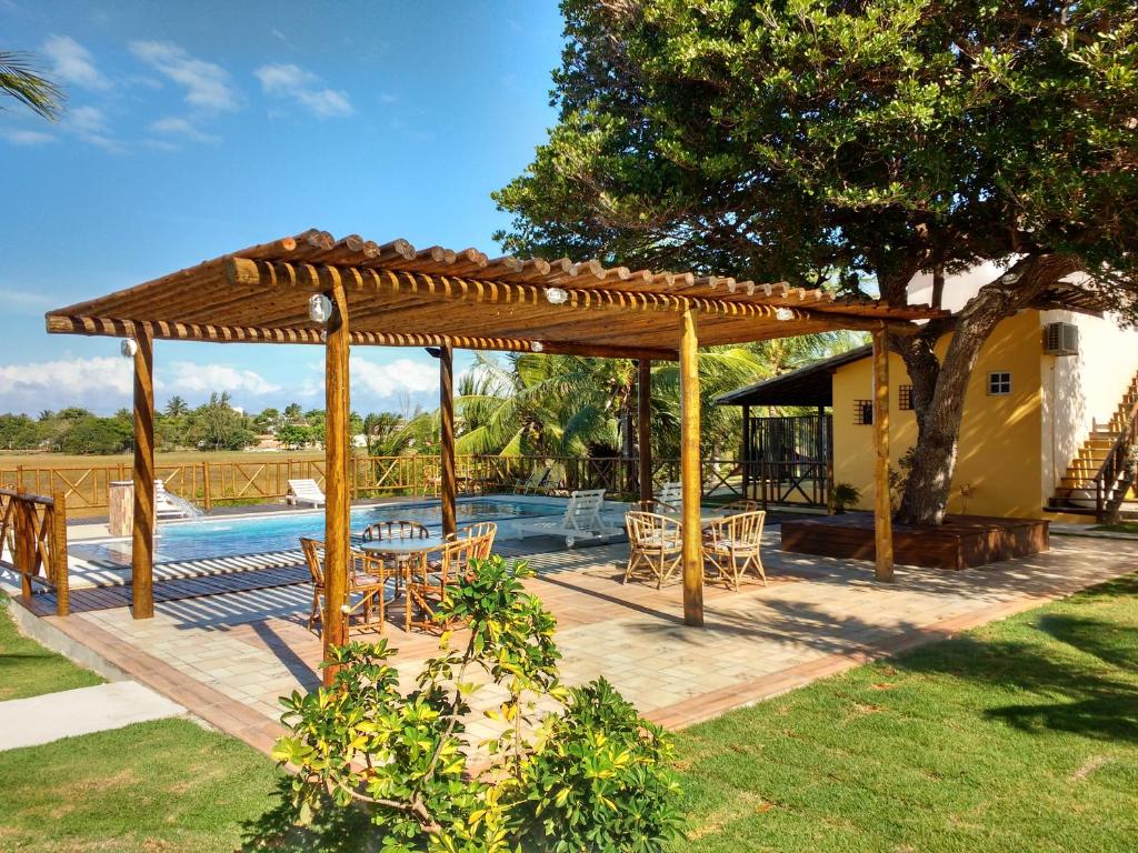 a wooden pergola with tables and chairs next to a pool at Pousada Ilha do Meio in Itacimirim