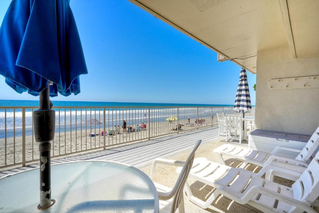 a table with chairs and an umbrella on the beach at Oceanfront 2BR - Private Patio - Steps to Beach in Carlsbad