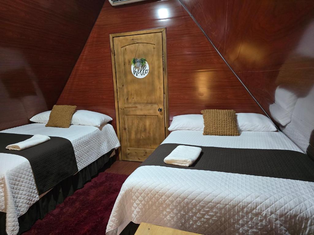 a room with two beds and a wooden wall at Cabañas Villa Aurora in Campamento