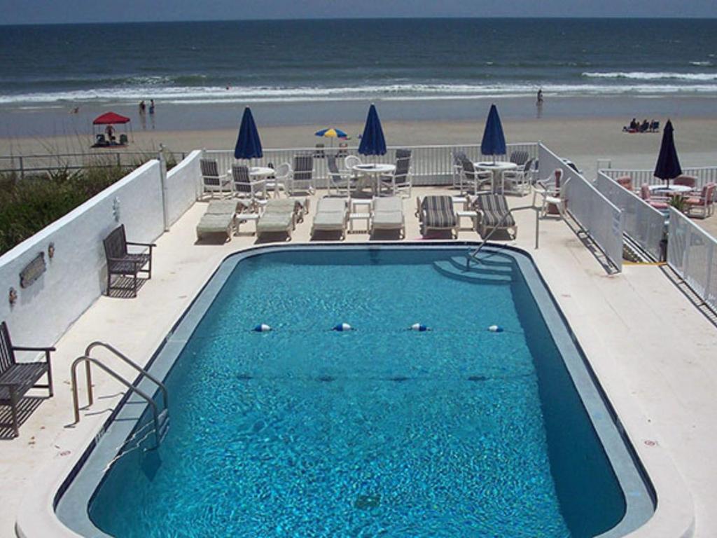 a swimming pool next to a beach with chairs and umbrellas at Sierra Suites in Daytona Beach