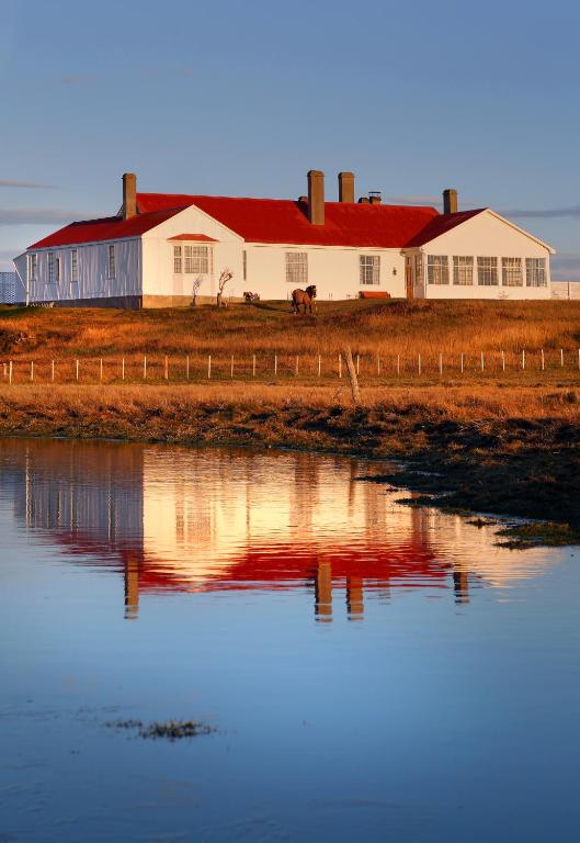 a white barn with a red roof reflected in the water at Hotel Estancia Caleta Josefina in Onaisin