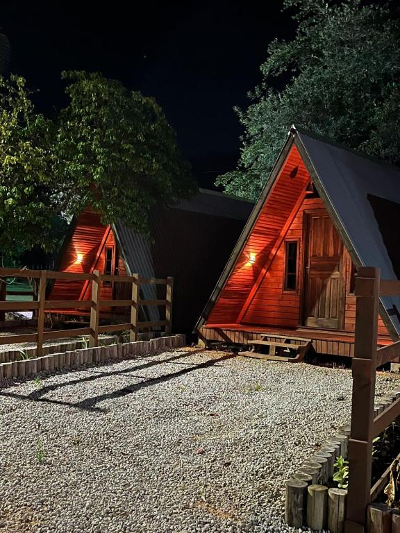 two small wooden huts with a fence and gravel at Pousada Vale das Pedras 02 in Pedras Grandes