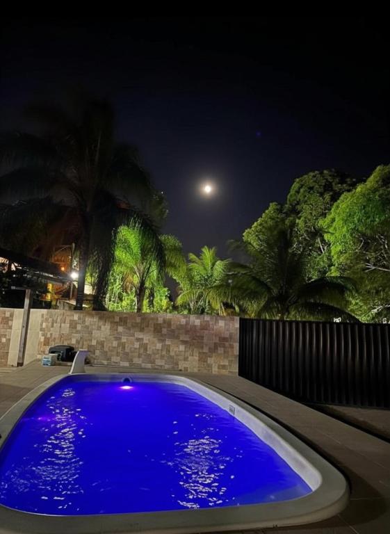 a blue swimming pool at night with a fence and trees at Casa Shekinah in Araruama