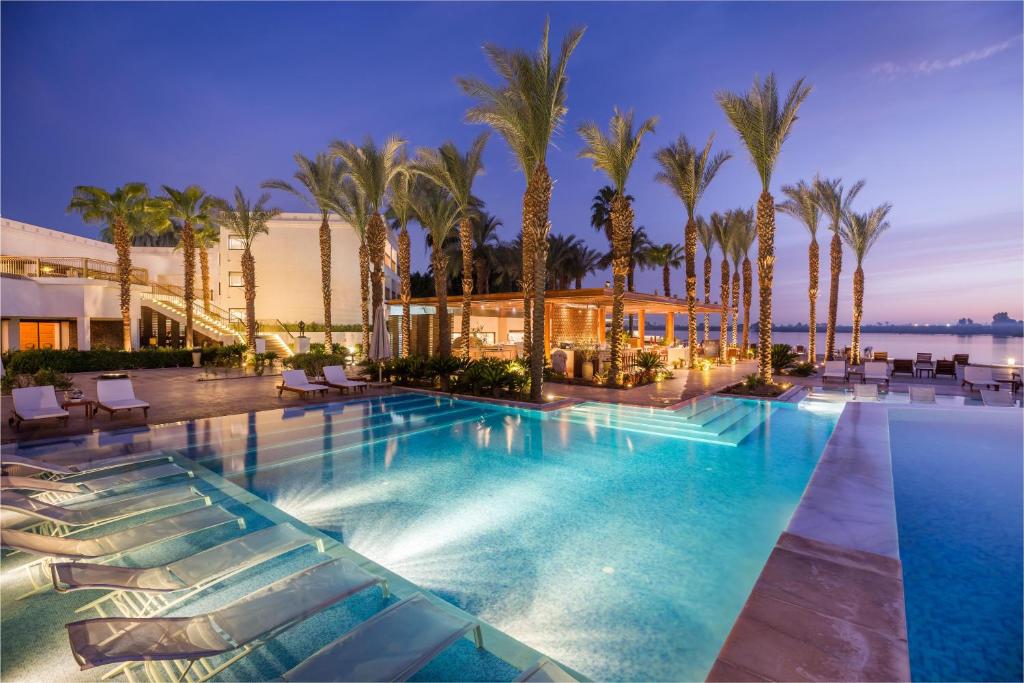 a swimming pool with palm trees and a building at Hilton Luxor Resort & Spa in Luxor