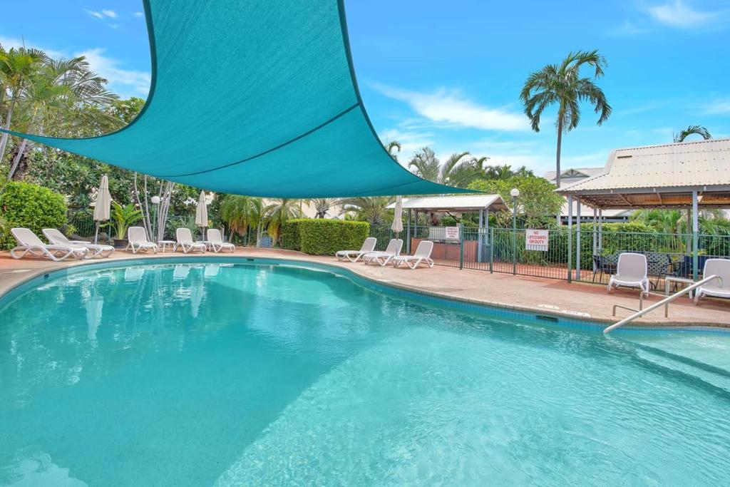 a large swimming pool with chairs and a umbrella over it at Sunset Escape in Broome