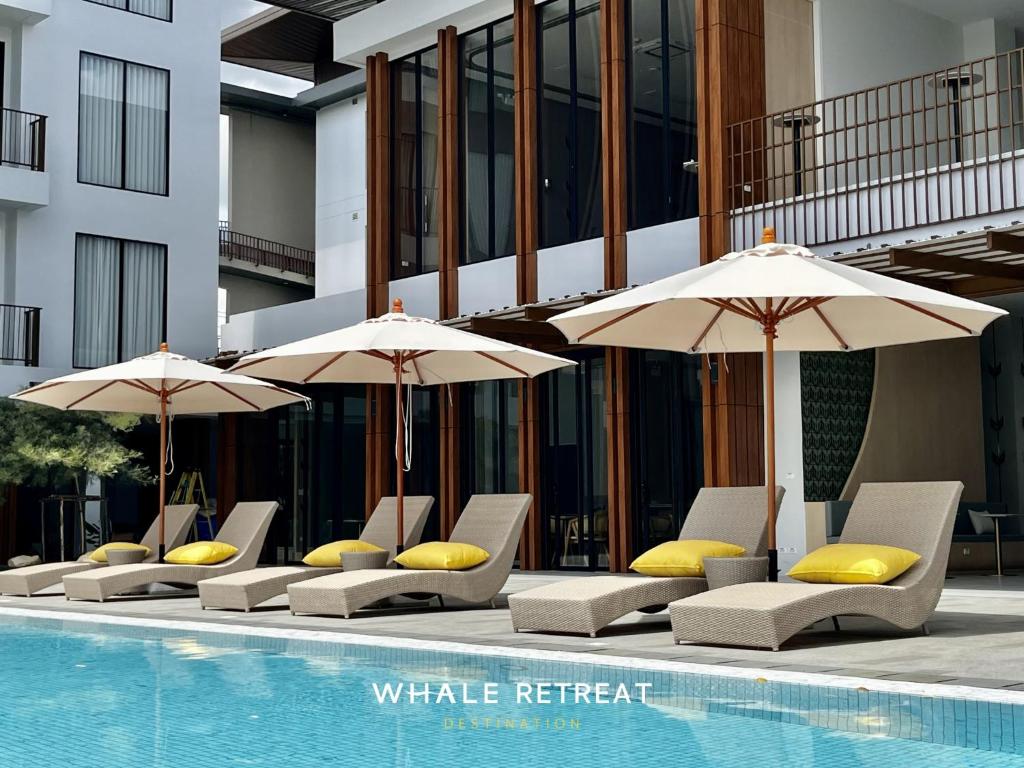 a group of chairs with umbrellas next to a pool at Whale Retreat Destination in Hat Yai
