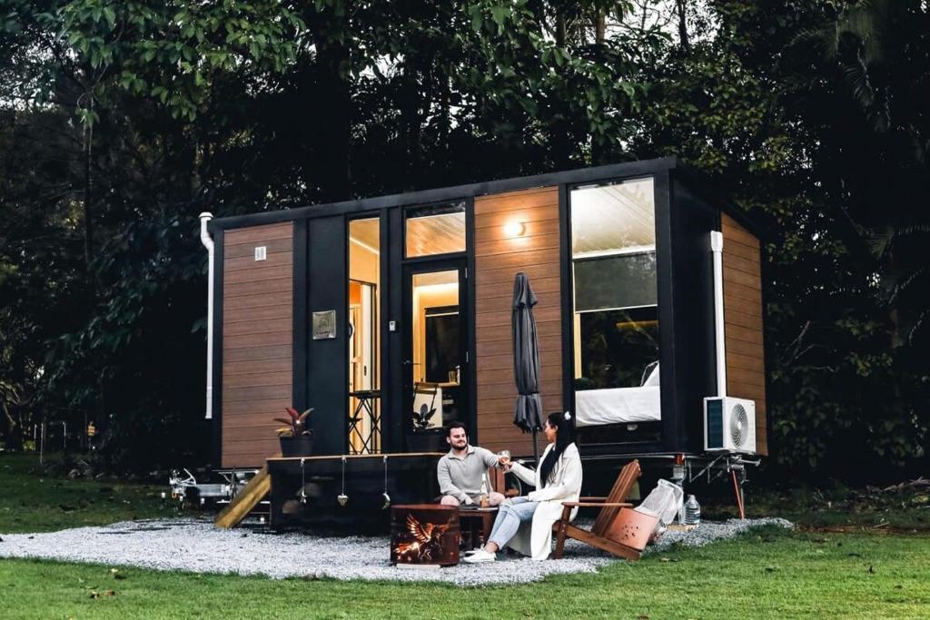 two people sitting on a bench in front of a tiny house at Hinterland Hideout by Tiny Away in Myocum