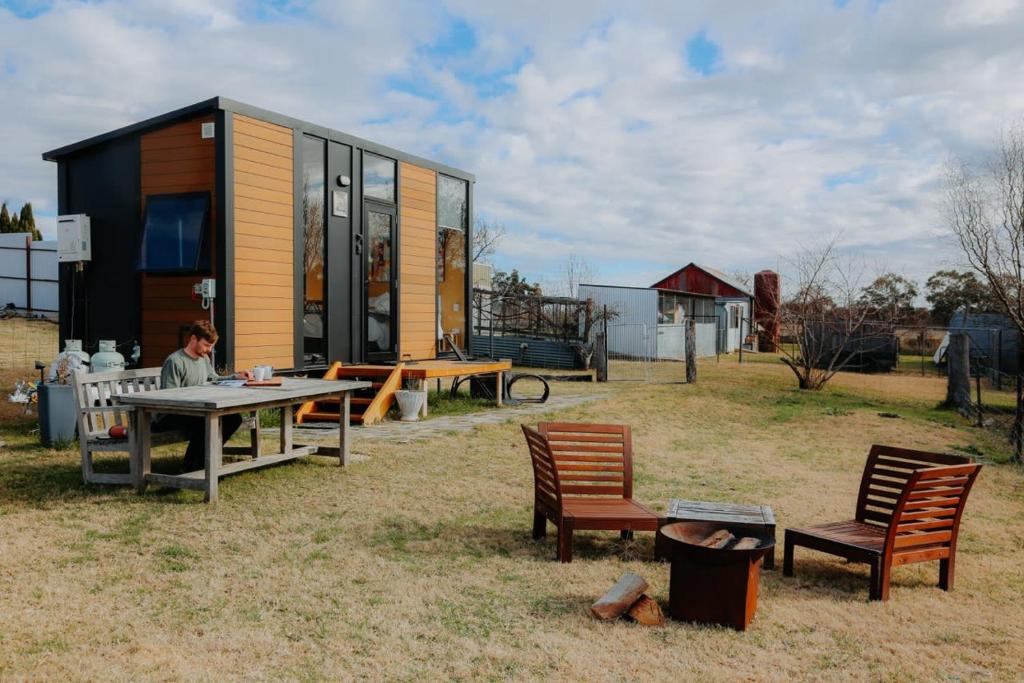 a woman sitting at a table in front of a tiny house at Tiny Boorowa by Tiny Away in Boorowa